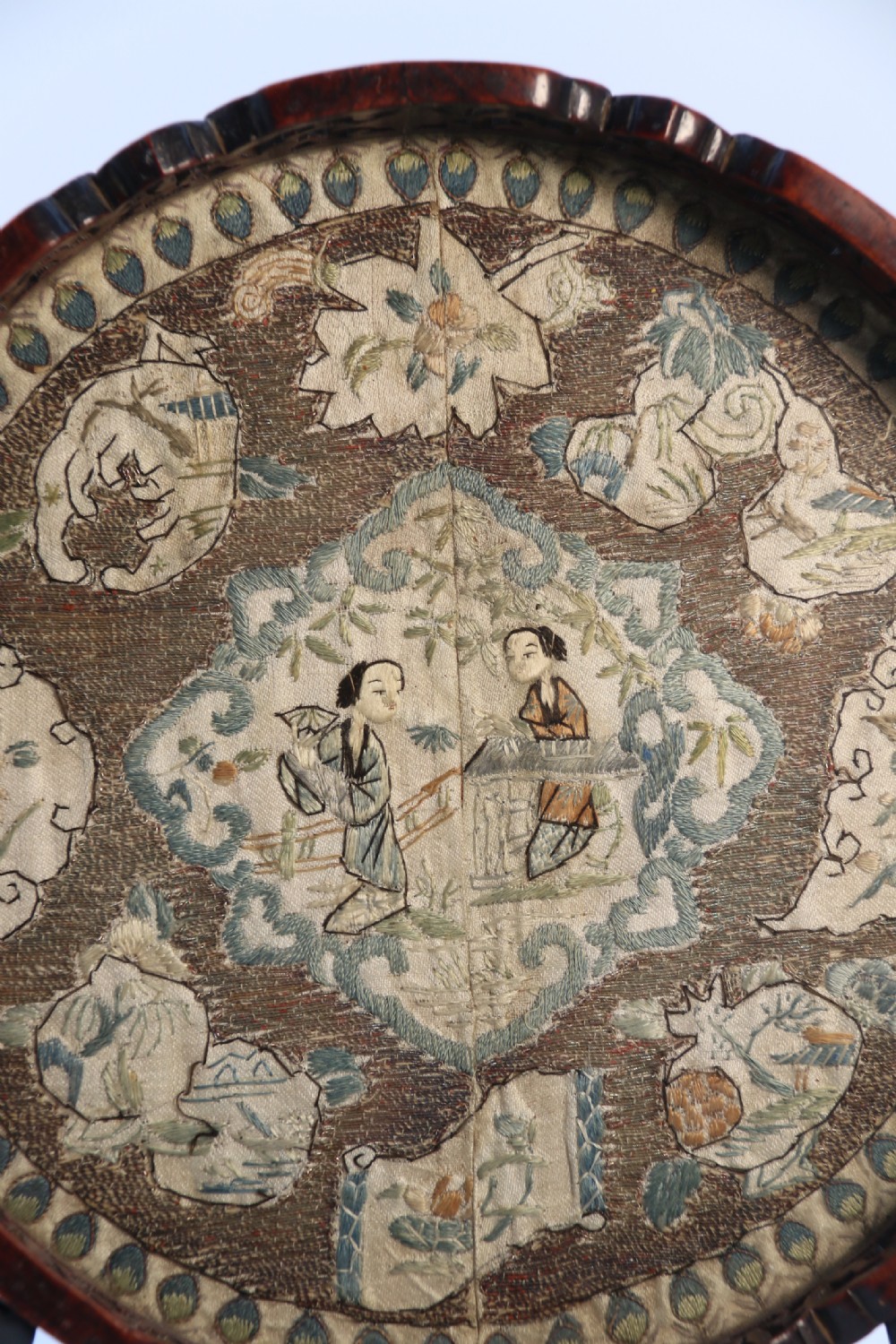A circular carved dark hardwood tray containing an inset 19th-century Chinese silk embroidery with figural and botanical motifs. View V