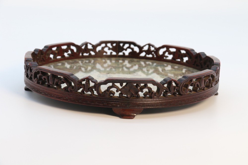 A circular carved dark hardwood tray containing an inset 19th-century Chinese silk embroidery with figural and botanical motifs. View X