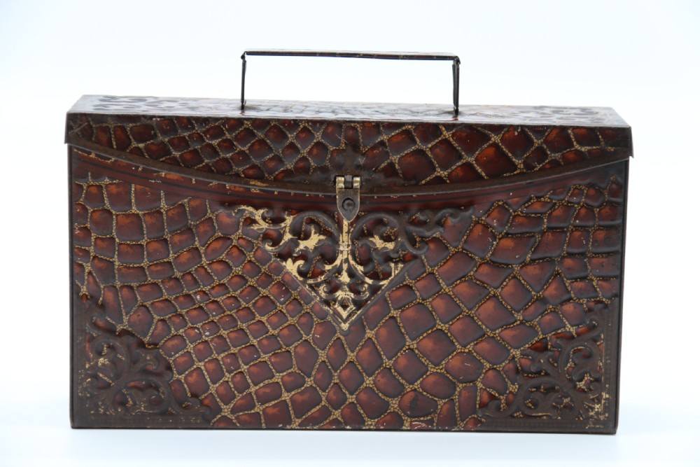 A rectangular metal novelty biscuit tin shaped like a leather satchel with printed crocodile texture, gold scroll accents, and a top carrying handle. View II