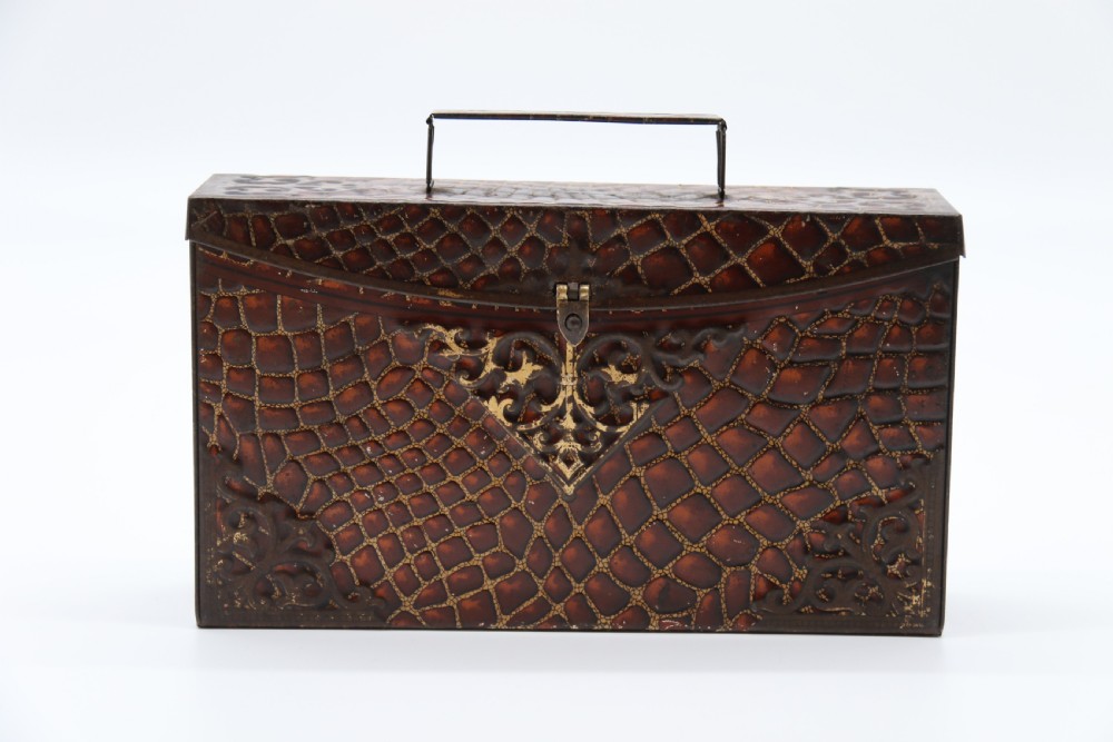 A rectangular metal novelty biscuit tin shaped like a leather satchel with printed crocodile texture, gold scroll accents, and a top carrying handle. View III