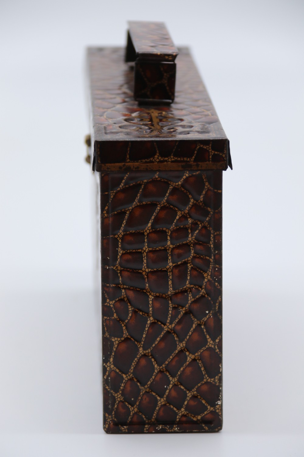 A rectangular metal novelty biscuit tin shaped like a leather satchel with printed crocodile texture, gold scroll accents, and a top carrying handle. View V