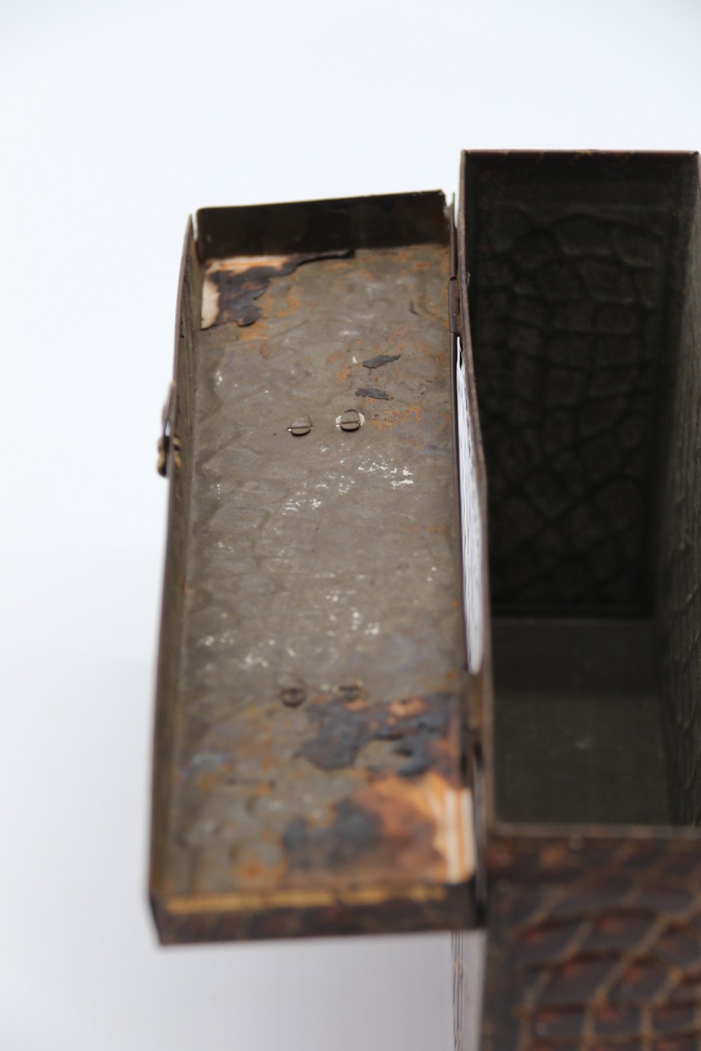 A rectangular metal novelty biscuit tin shaped like a leather satchel with printed crocodile texture, gold scroll accents, and a top carrying handle. View XI