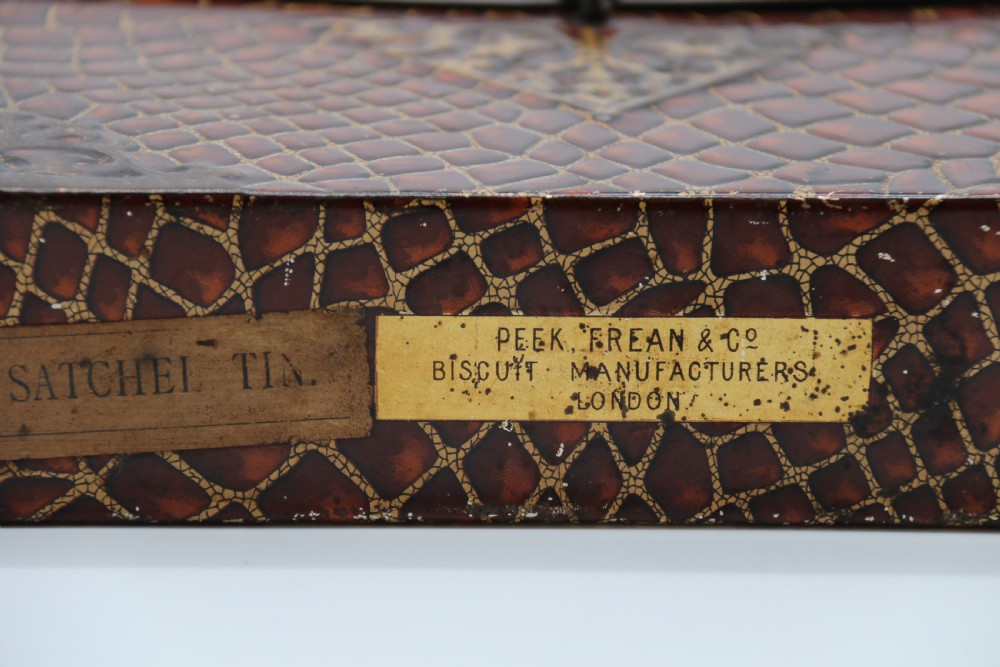 A rectangular metal novelty biscuit tin shaped like a leather satchel with printed crocodile texture, gold scroll accents, and a top carrying handle. View XIII