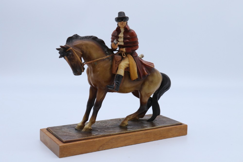 An Art Deco cold-painted metal figure of a masked highwayman on horseback mounted on a rectangular wooden plinth, featuring an integrated table lighter mechanism. View XVIII
