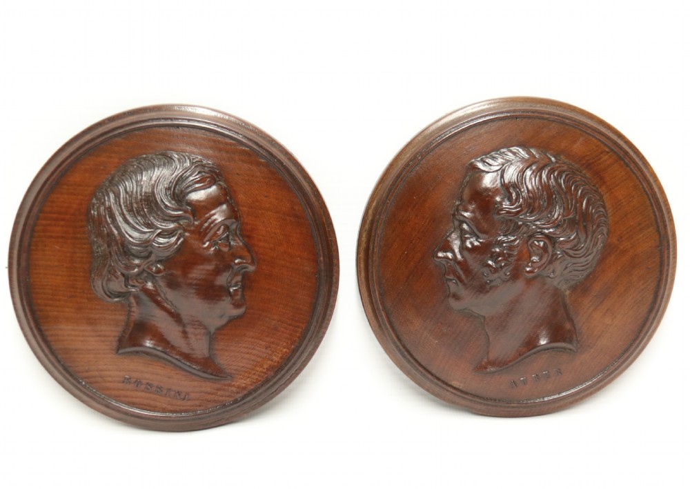 A pair of circular carved mahogany wall plaques featuring raised profile relief busts of classical composers Rossini and Auber.