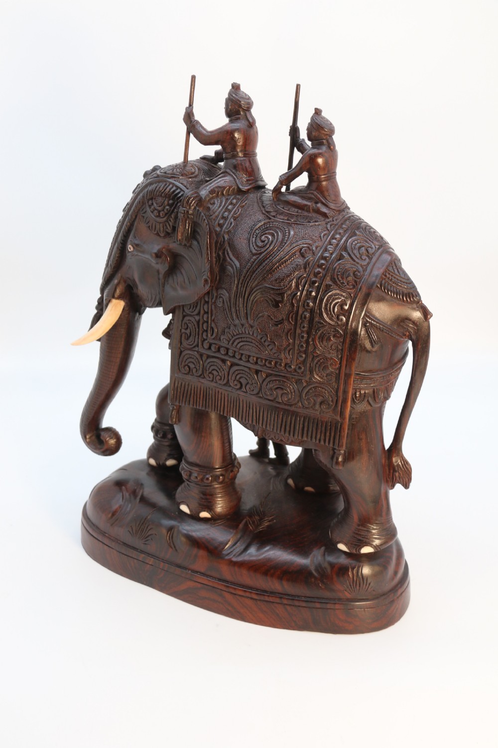 A dark hardwood sculpture depicting a ceremonial elephant adorned with decorative drapery accompanied by three mahouts on an integrated wooden base. View V