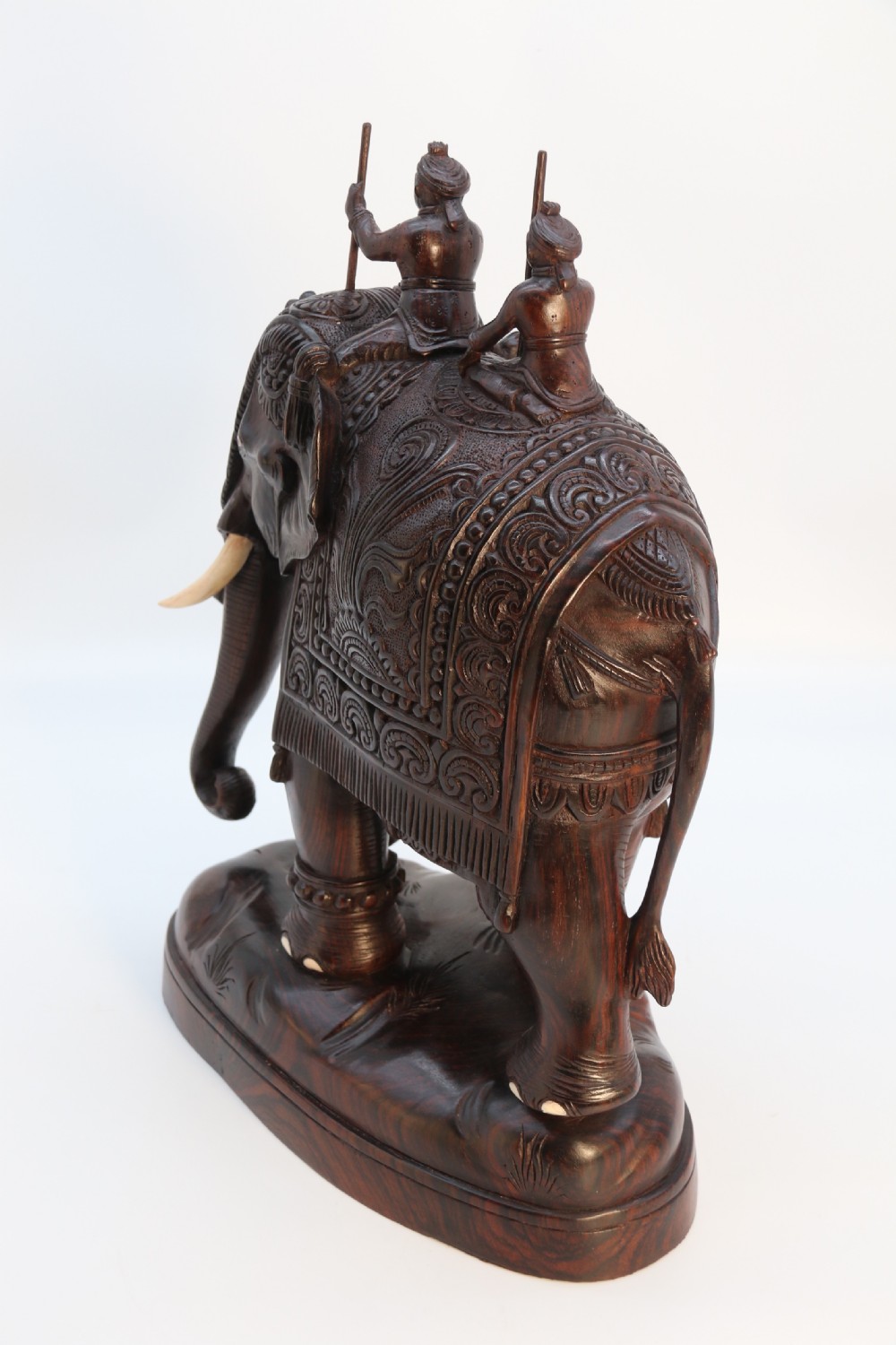 A dark hardwood sculpture depicting a ceremonial elephant adorned with decorative drapery accompanied by three mahouts on an integrated wooden base. View VI