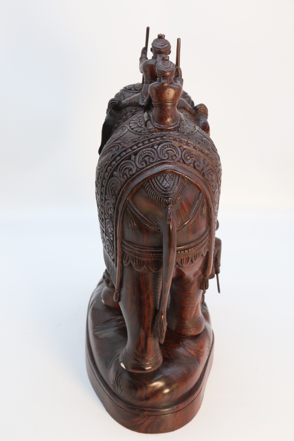 A dark hardwood sculpture depicting a ceremonial elephant adorned with decorative drapery accompanied by three mahouts on an integrated wooden base. View VII