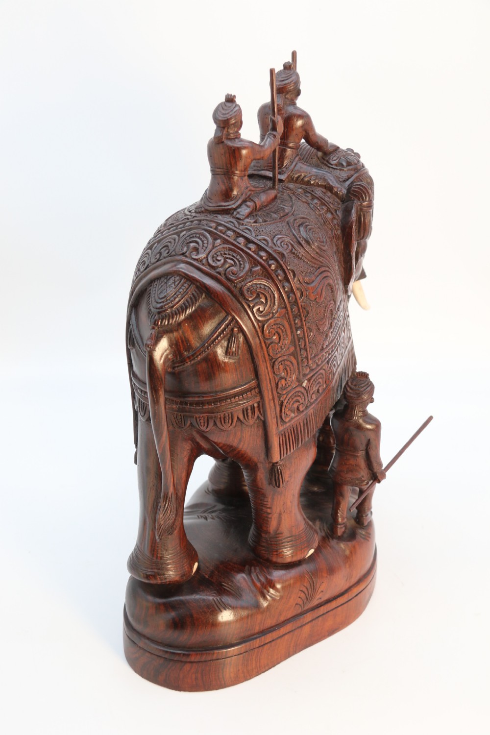A dark hardwood sculpture depicting a ceremonial elephant adorned with decorative drapery accompanied by three mahouts on an integrated wooden base. View VIII