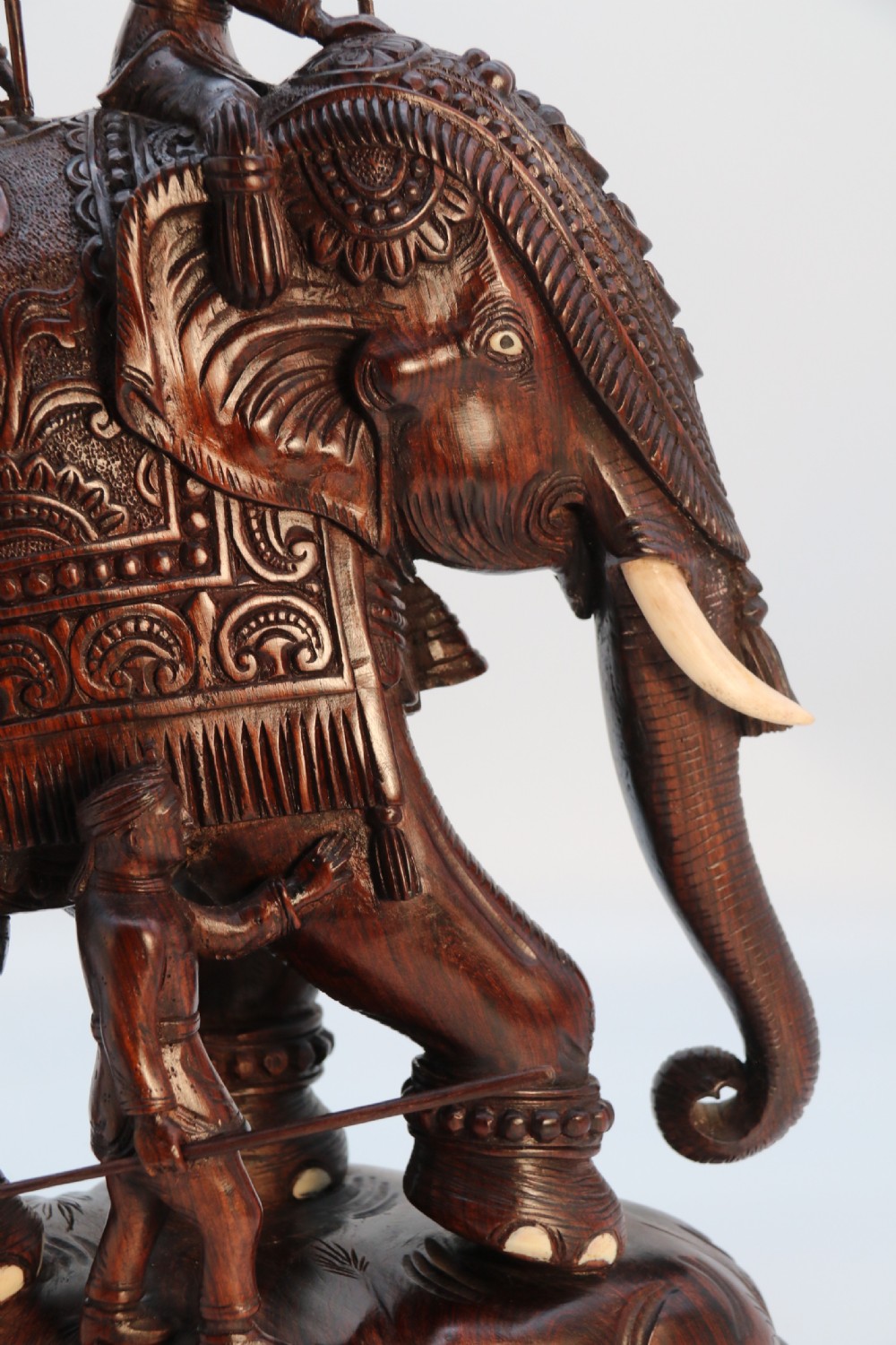 A dark hardwood sculpture depicting a ceremonial elephant adorned with decorative drapery accompanied by three mahouts on an integrated wooden base. View XII