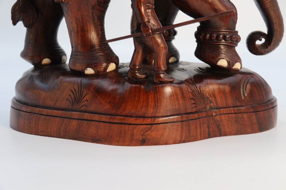 A dark hardwood sculpture depicting a ceremonial elephant adorned with decorative drapery accompanied by three mahouts on an integrated wooden base. View XIII