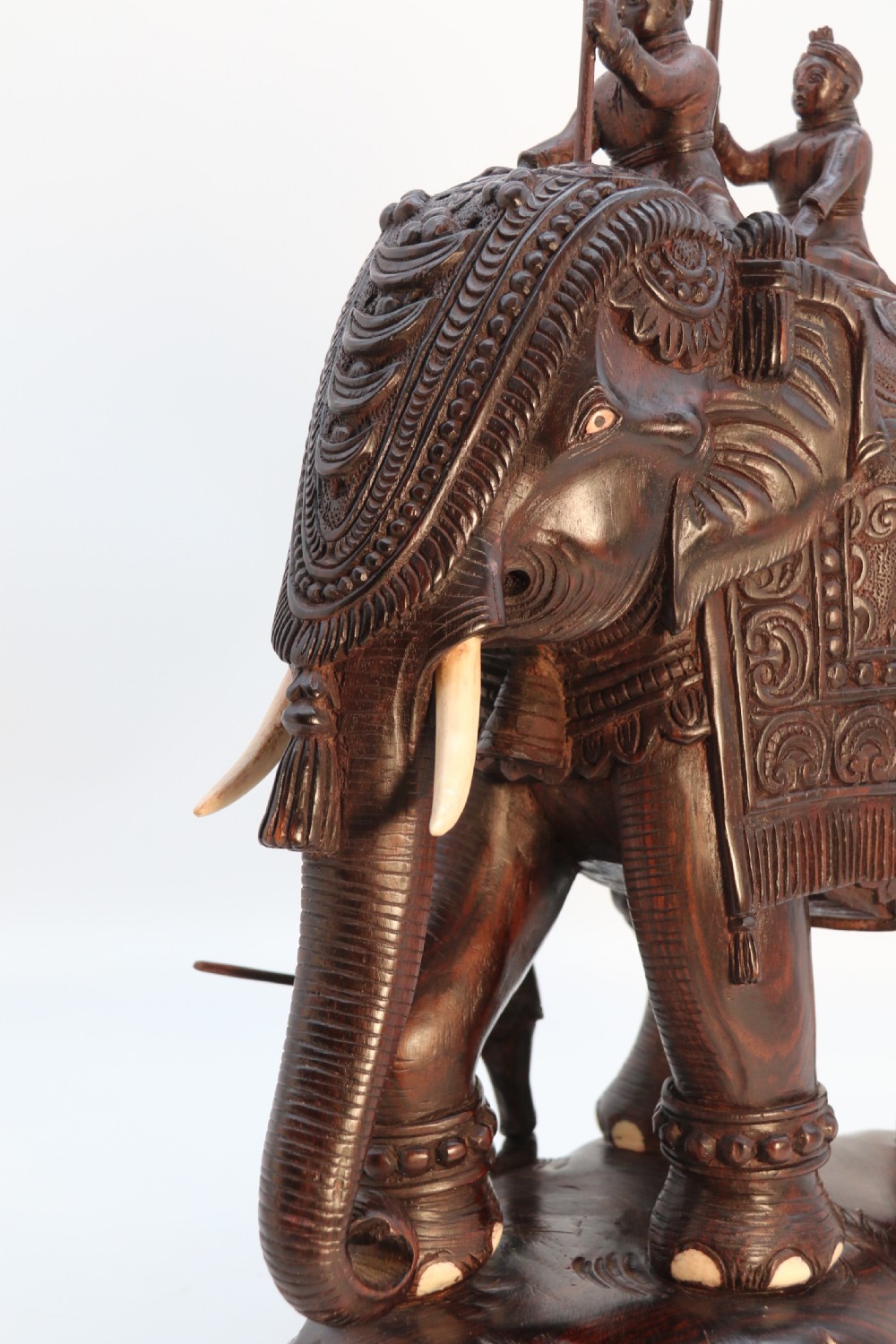 A dark hardwood sculpture depicting a ceremonial elephant adorned with decorative drapery accompanied by three mahouts on an integrated wooden base. View XVII