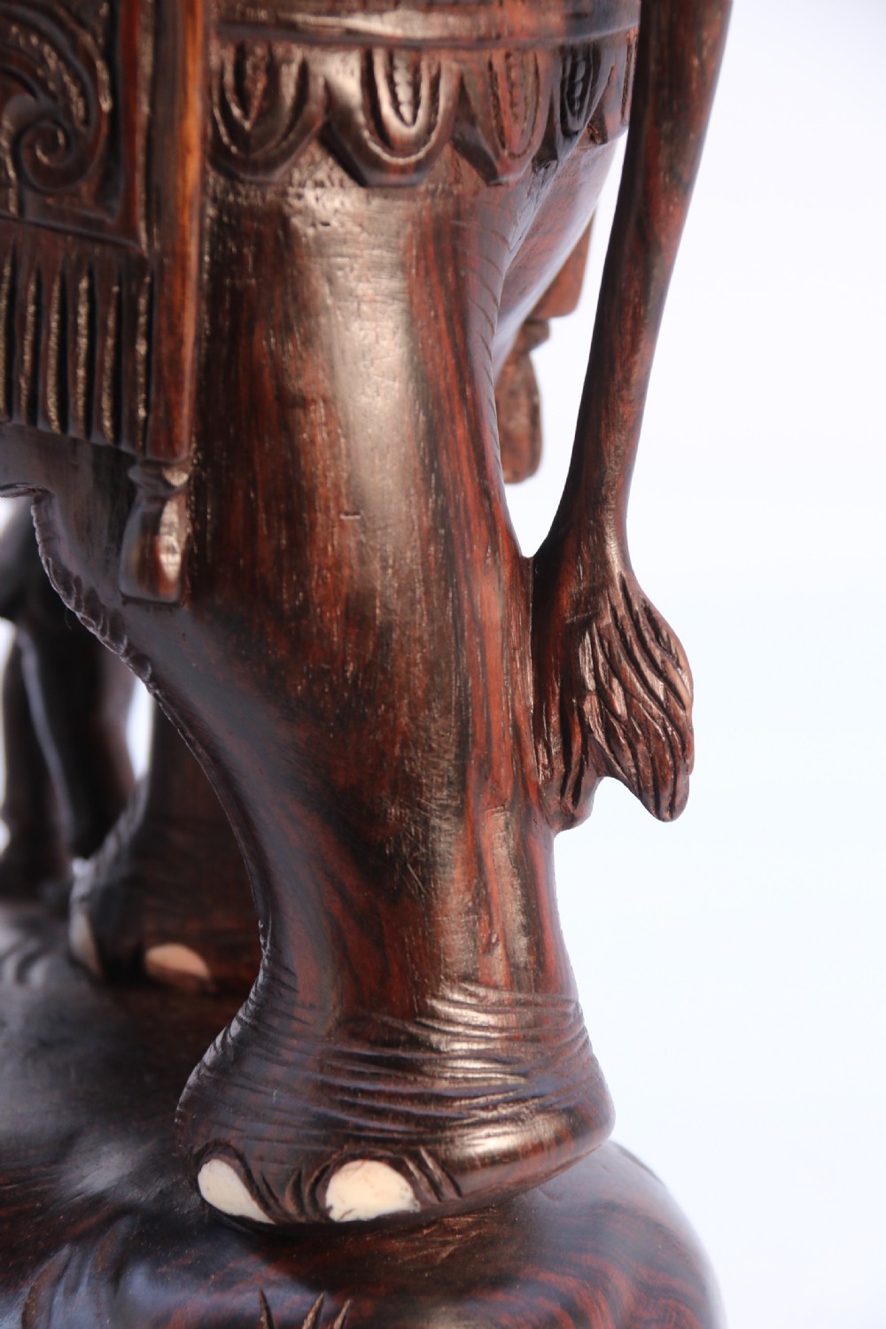 A dark hardwood sculpture depicting a ceremonial elephant adorned with decorative drapery accompanied by three mahouts on an integrated wooden base. View XX