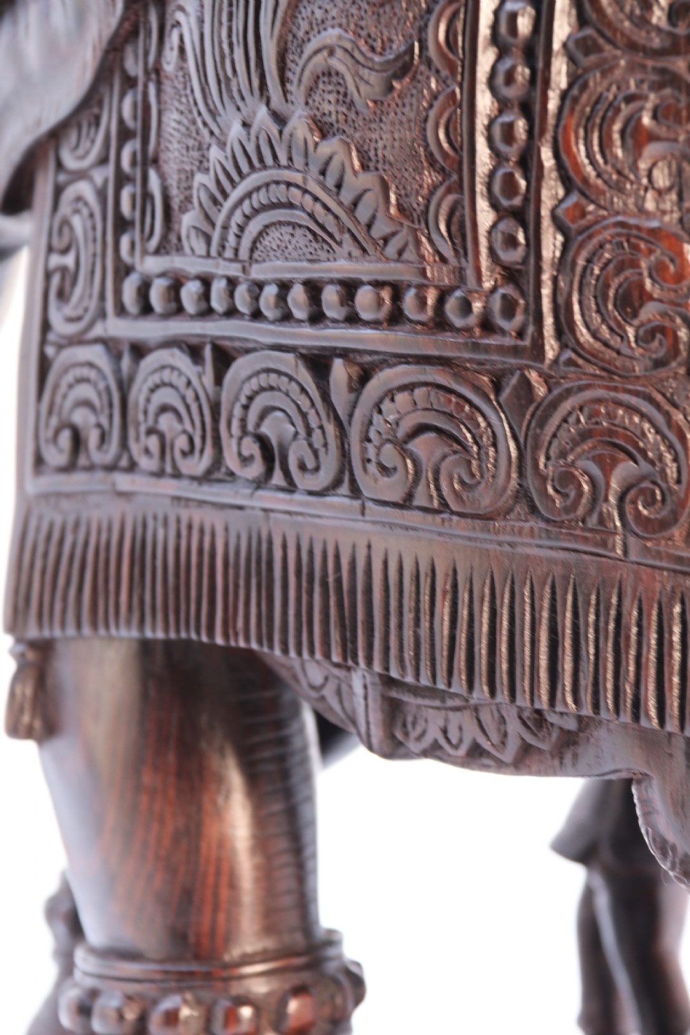 A dark hardwood sculpture depicting a ceremonial elephant adorned with decorative drapery accompanied by three mahouts on an integrated wooden base. View XXI