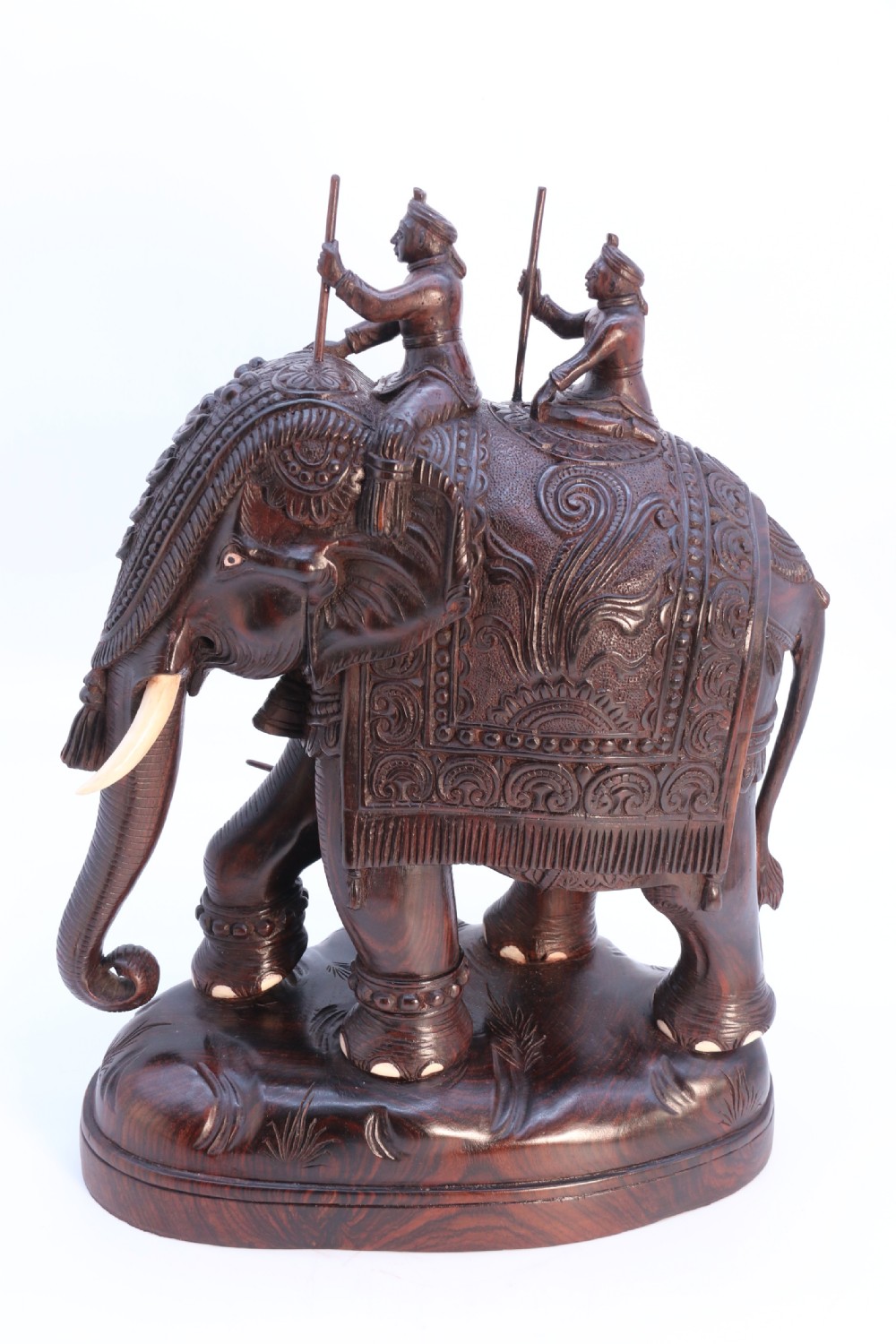 A dark hardwood sculpture depicting a ceremonial elephant adorned with decorative drapery accompanied by three mahouts on an integrated wooden base. View XXIV