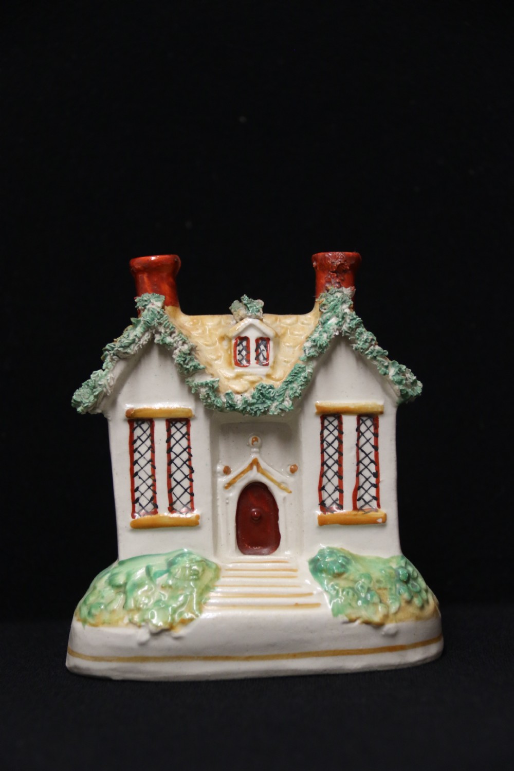 A 19th-century Staffordshire earthenware money box sculpted as a two-chimney cottage featuring applied shredded-clay foliage.