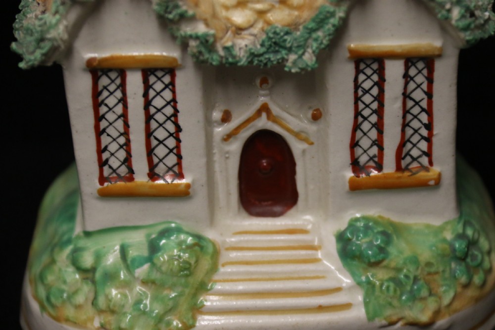 A 19th-century Staffordshire earthenware money box sculpted as a two-chimney cottage featuring applied shredded-clay foliage. View VI