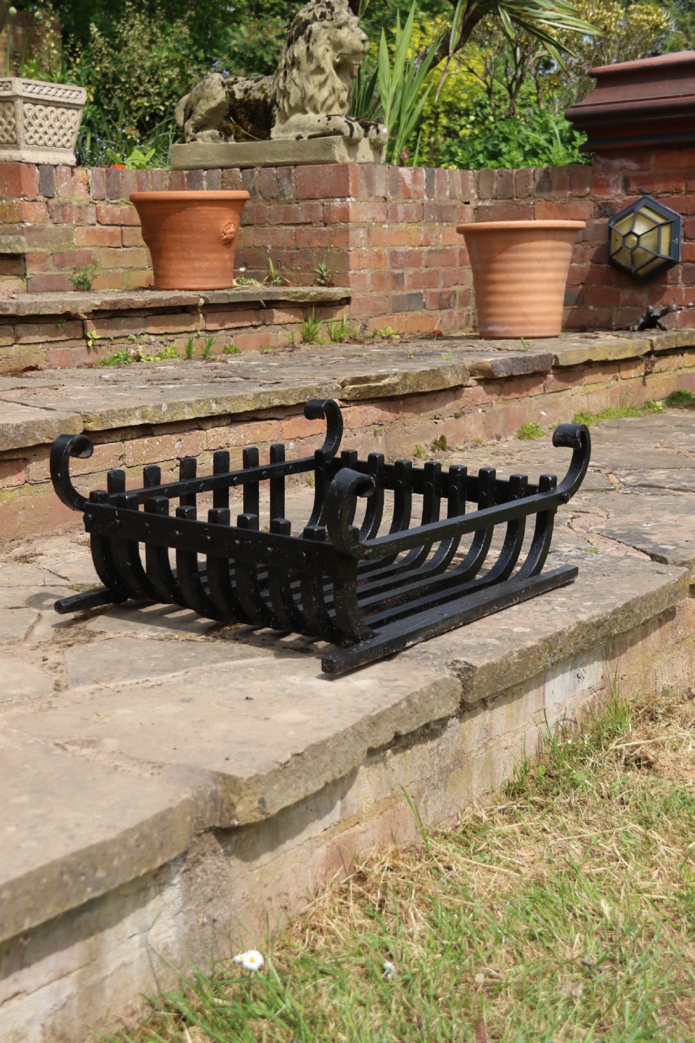 A black wrought iron fire basket featuring a curved slatted log cradle, scrolled corner terminals, and riveted front bars. View XVI