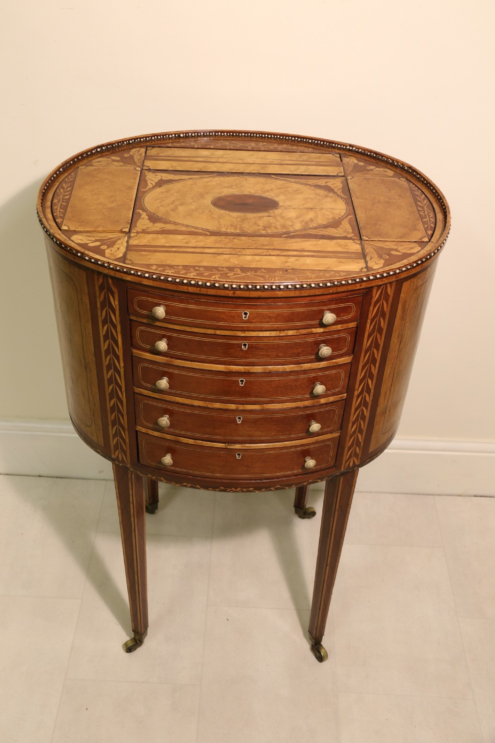 An oval George III satinwood worktable featuring marquetry inlay, multiple drawers, tapered legs, and a rising mirror compartment. View II