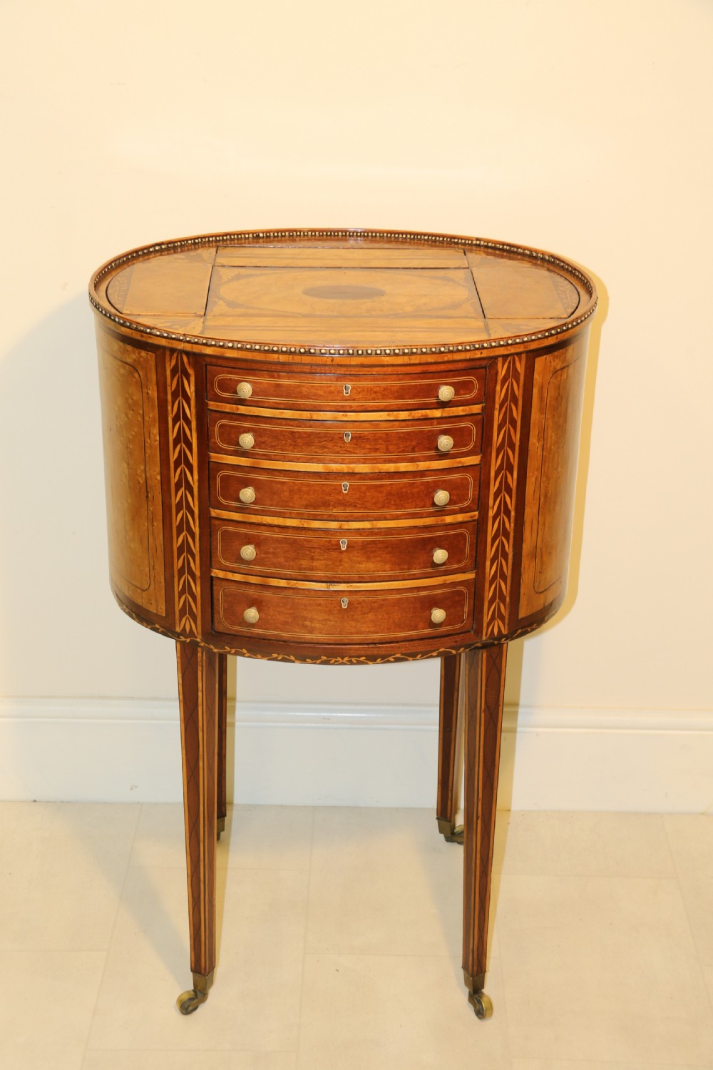 An oval George III satinwood worktable featuring marquetry inlay, multiple drawers, tapered legs, and a rising mirror compartment. View III