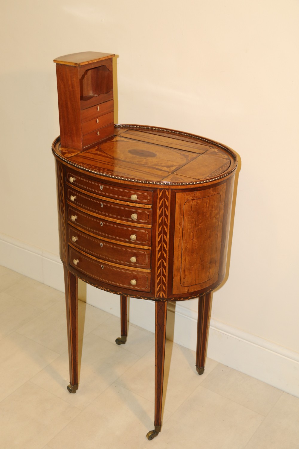 An oval George III satinwood worktable featuring marquetry inlay, multiple drawers, tapered legs, and a rising mirror compartment. View XII
