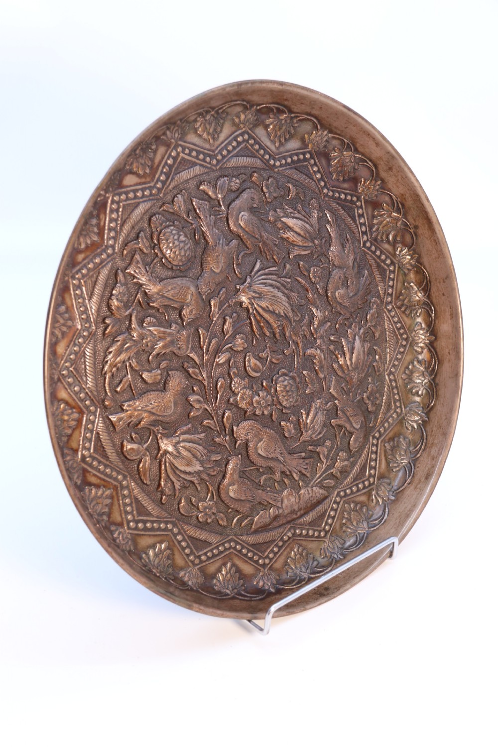 A circular copper repousse charger featuring relief carvings of birds, flowers, and geometric borders. View II
