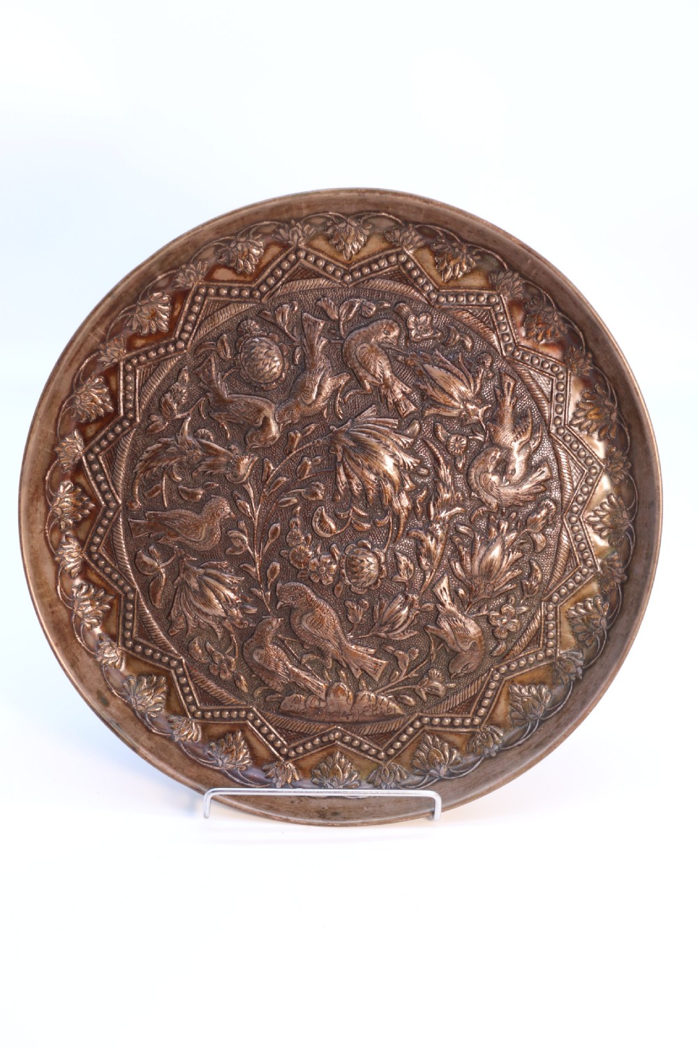 A circular copper repousse charger featuring relief carvings of birds, flowers, and geometric borders. View III