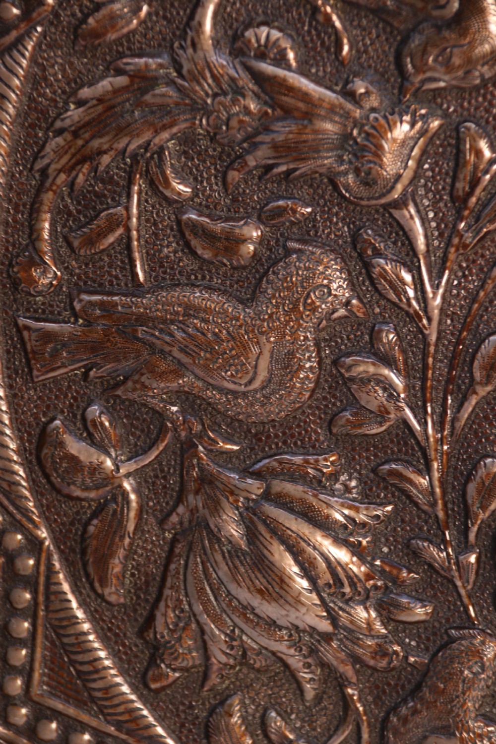 A circular copper repousse charger featuring relief carvings of birds, flowers, and geometric borders. View IV