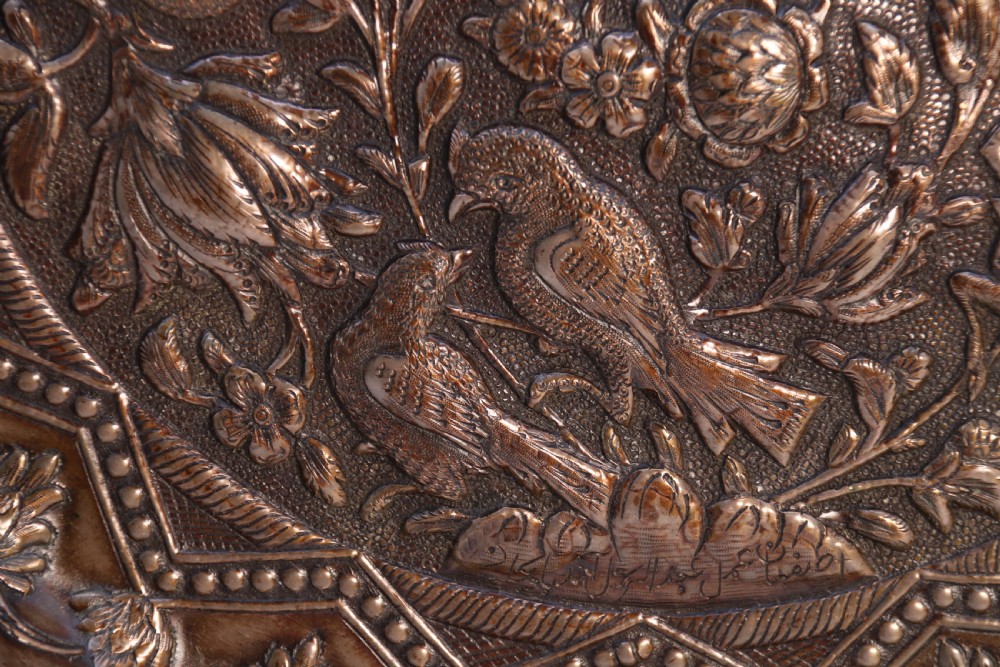 A circular copper repousse charger featuring relief carvings of birds, flowers, and geometric borders. View V