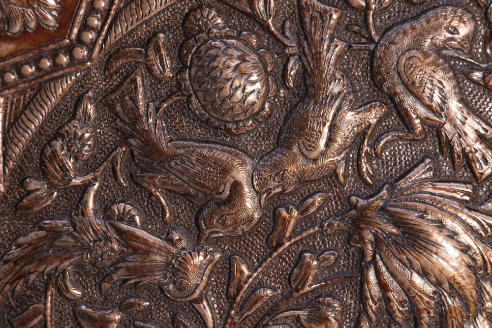 A circular copper repousse charger featuring relief carvings of birds, flowers, and geometric borders. View VI