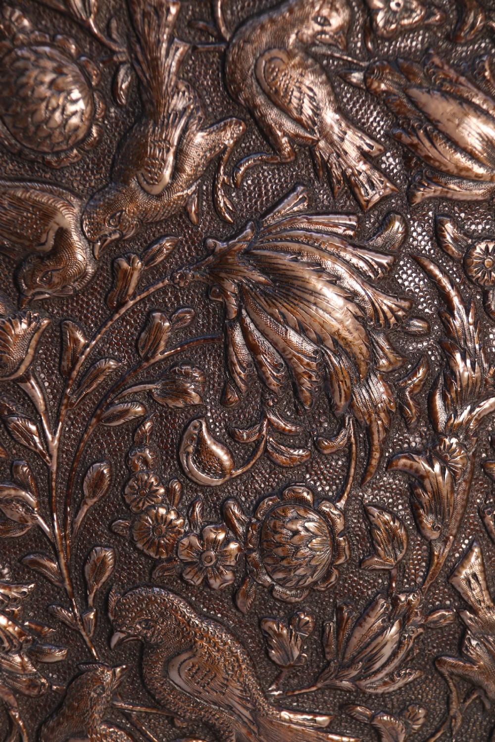 A circular copper repousse charger featuring relief carvings of birds, flowers, and geometric borders. View VII