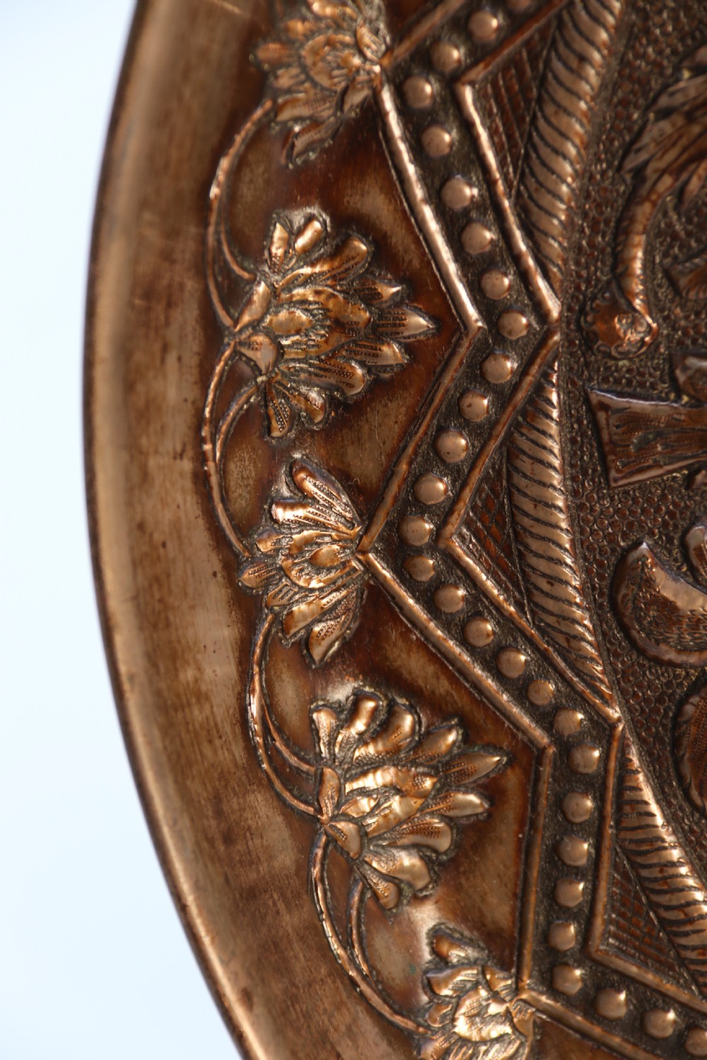A circular copper repousse charger featuring relief carvings of birds, flowers, and geometric borders. View VIII