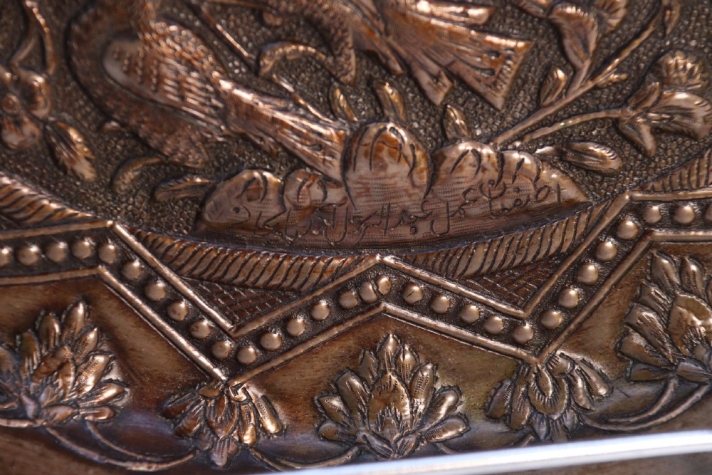 A circular copper repousse charger featuring relief carvings of birds, flowers, and geometric borders. View IX