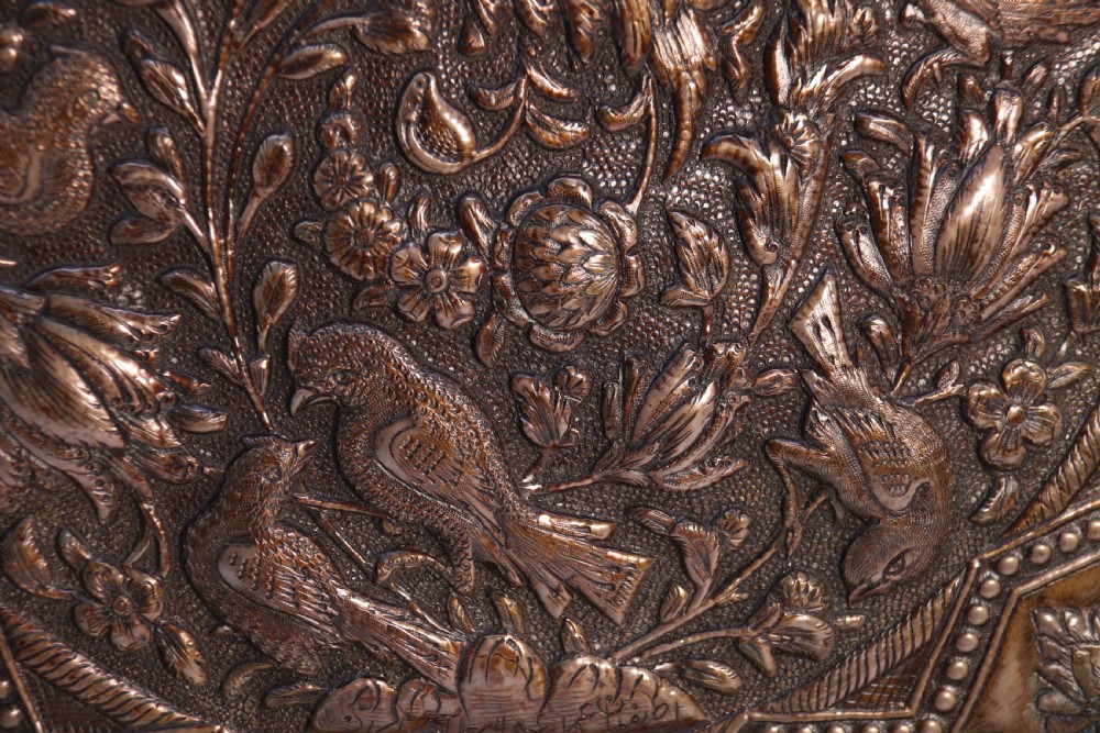 A circular copper repousse charger featuring relief carvings of birds, flowers, and geometric borders. View X