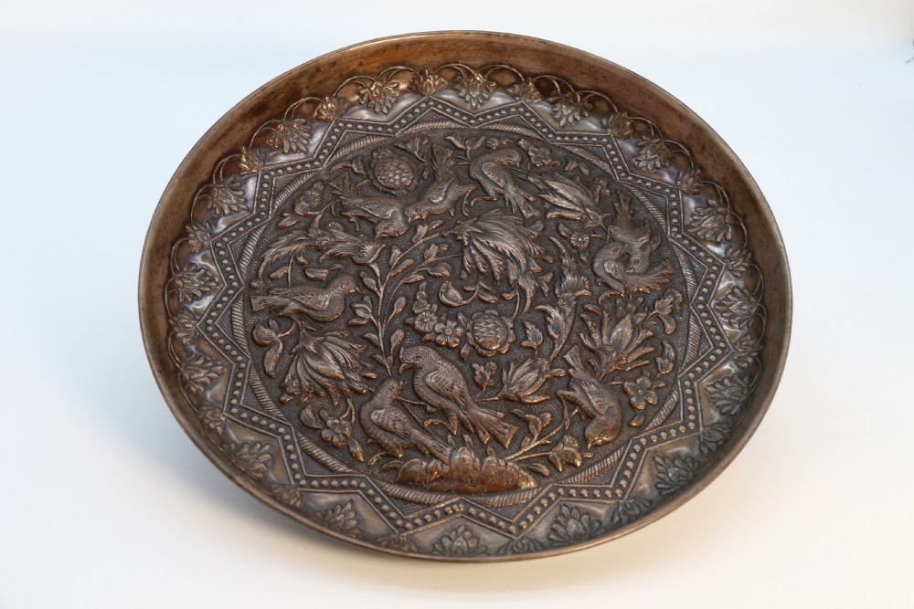 A circular copper repousse charger featuring relief carvings of birds, flowers, and geometric borders.