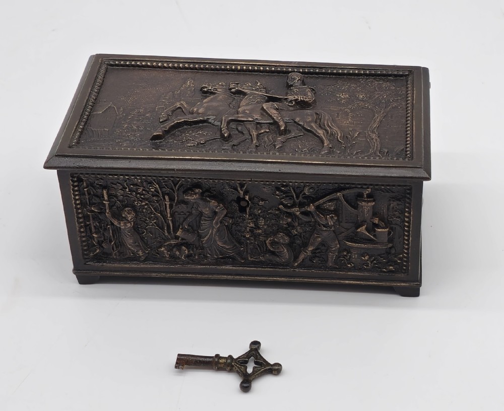 A rectangular dark patinated bronze jewellery casket featuring raised relief scenes on the sides and lid, accompanied by a small decorative key.