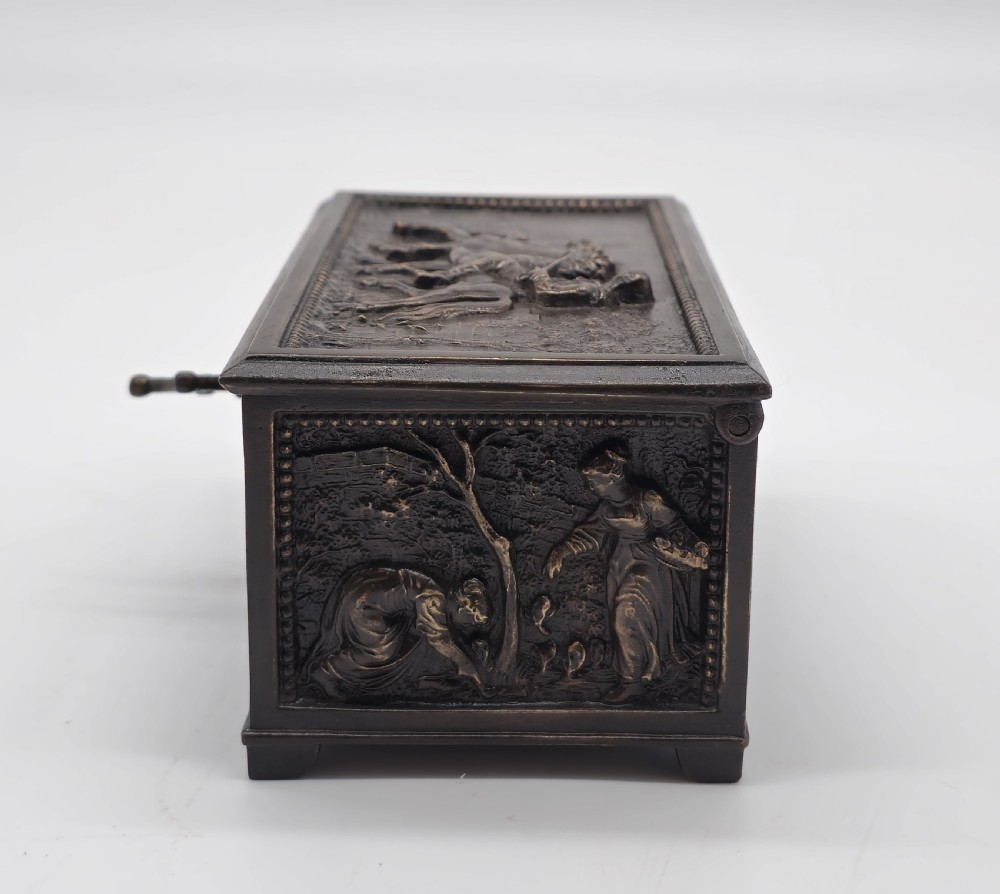 A rectangular dark patinated bronze jewellery casket featuring raised relief scenes on the sides and lid, accompanied by a small decorative key. View XIII