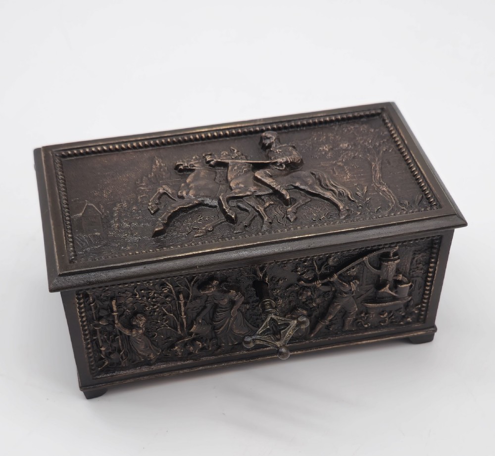 A rectangular dark patinated bronze jewellery casket featuring raised relief scenes on the sides and lid, accompanied by a small decorative key. View XIV