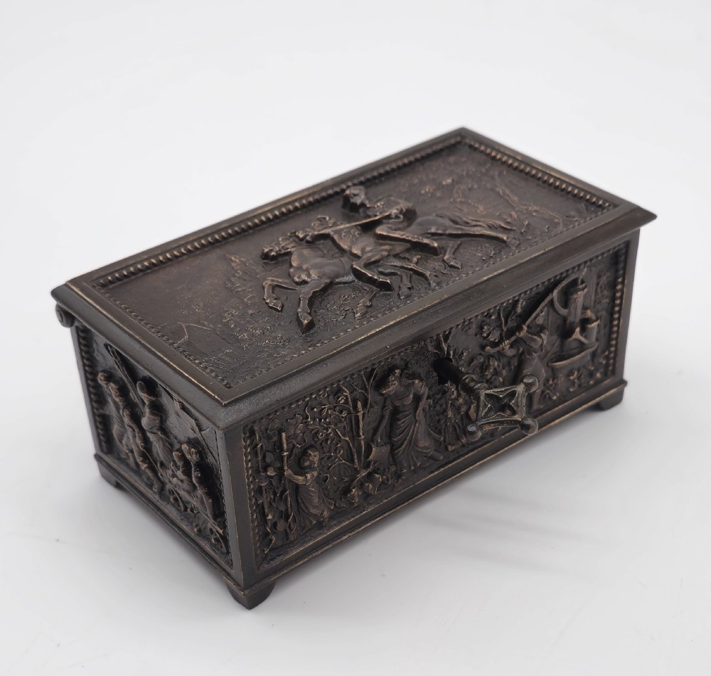 A rectangular dark patinated bronze jewellery casket featuring raised relief scenes on the sides and lid, accompanied by a small decorative key. View XV
