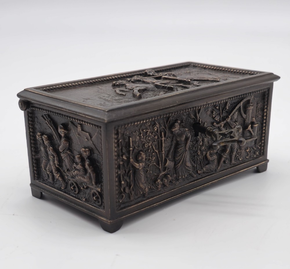 A rectangular dark patinated bronze jewellery casket featuring raised relief scenes on the sides and lid, accompanied by a small decorative key. View XVI