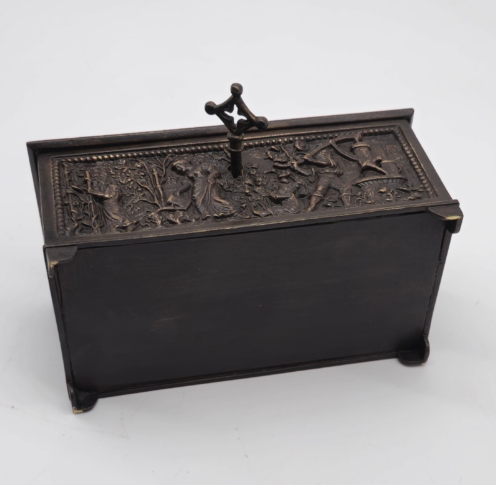 A rectangular dark patinated bronze jewellery casket featuring raised relief scenes on the sides and lid, accompanied by a small decorative key. View XVII