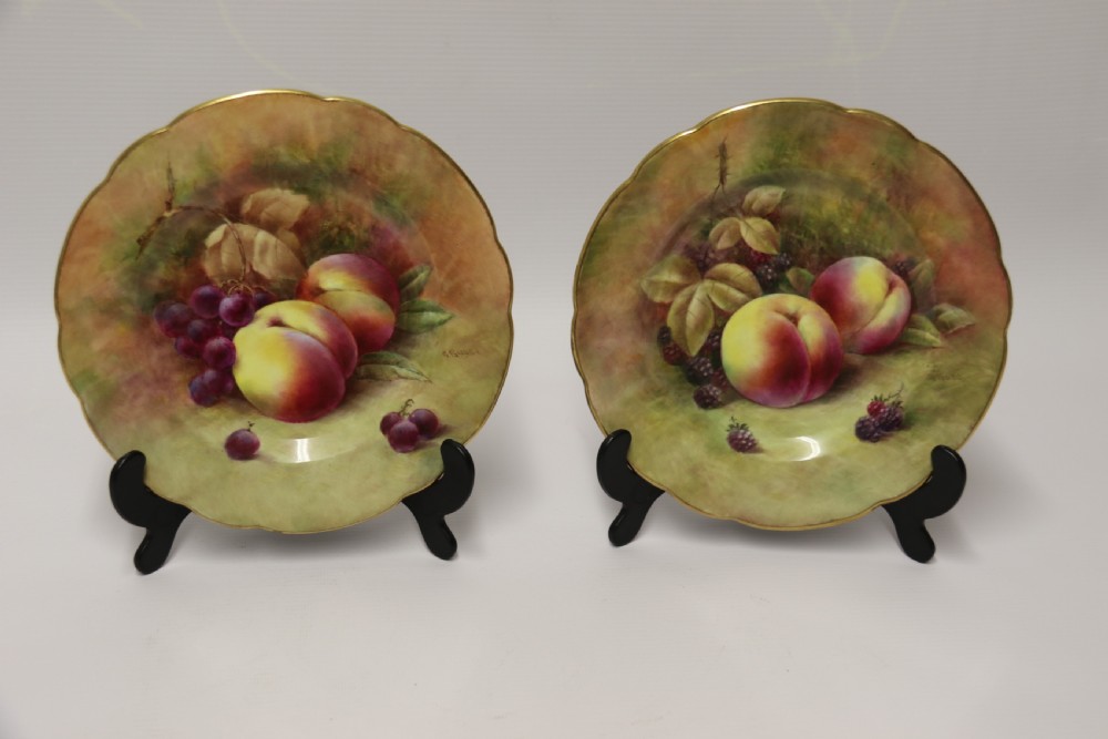 A pair of circular hand-painted porcelain plates displaying still life compositions of peaches, grapes, and blackberries framed by gilded scalloped edges. View II