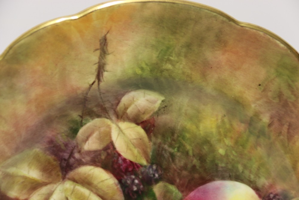 A pair of circular hand-painted porcelain plates displaying still life compositions of peaches, grapes, and blackberries framed by gilded scalloped edges. View X