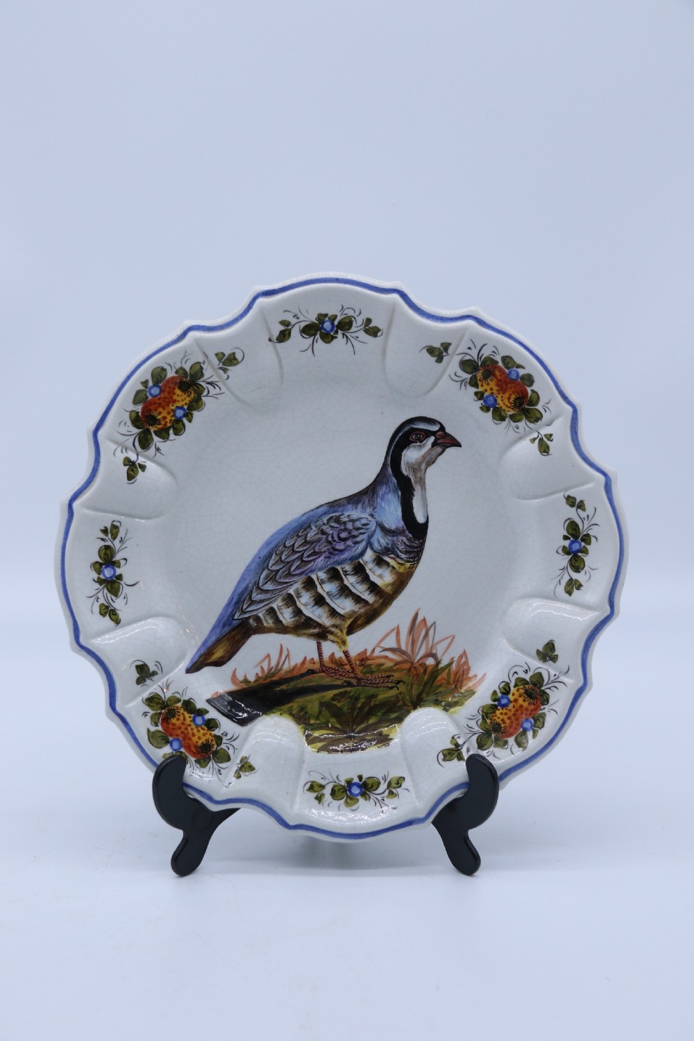 A circular tin-glazed earthenware wall charger featuring a hand-painted game bird in the centre surrounded by a scalloped, floral-decorated rim with blue edging.