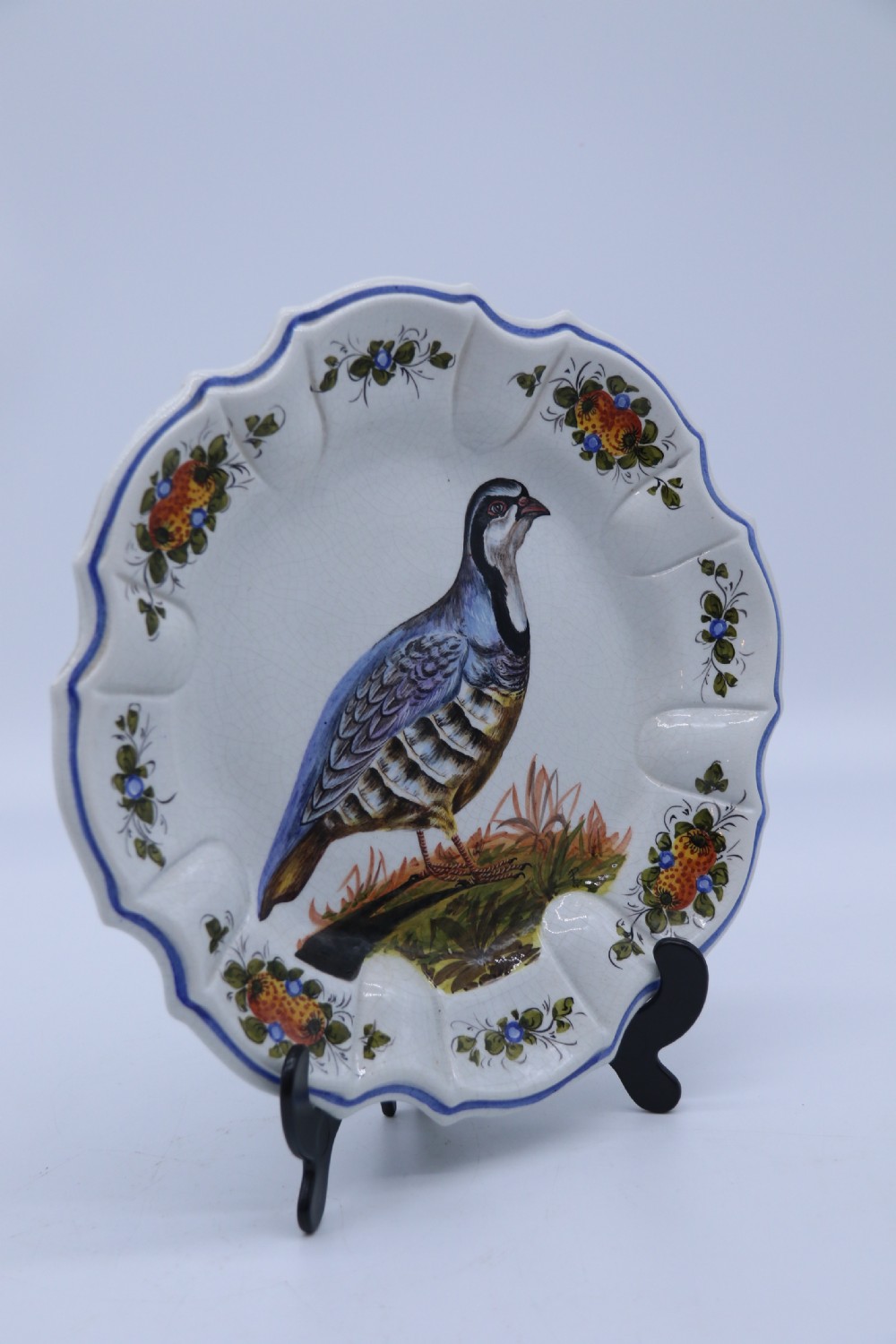A circular tin-glazed earthenware wall charger featuring a hand-painted game bird in the centre surrounded by a scalloped, floral-decorated rim with blue edging. View III
