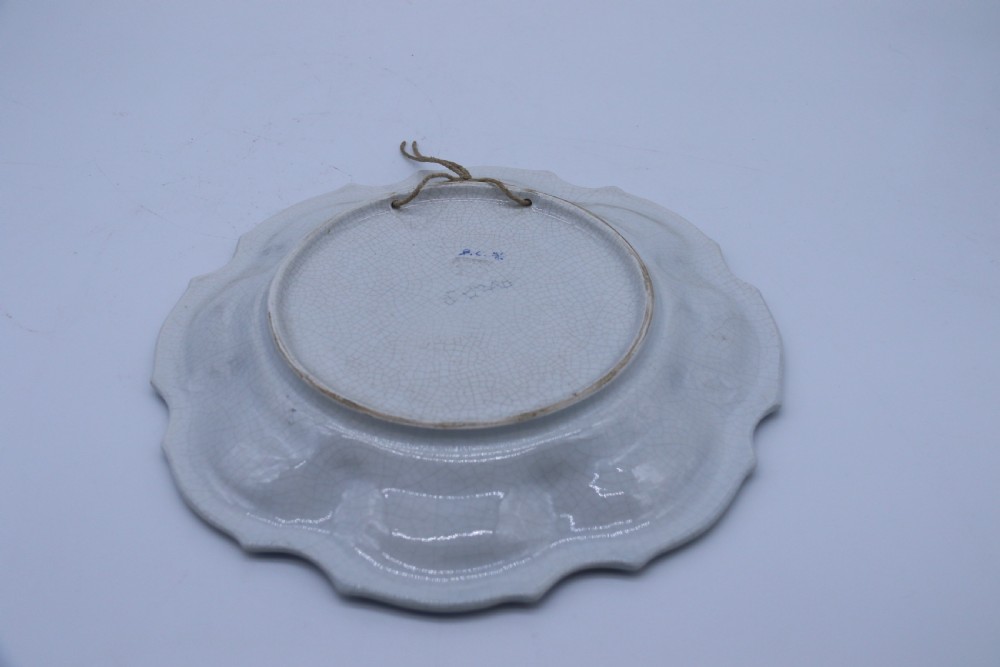 A circular tin-glazed earthenware wall charger featuring a hand-painted game bird in the centre surrounded by a scalloped, floral-decorated rim with blue edging. View V