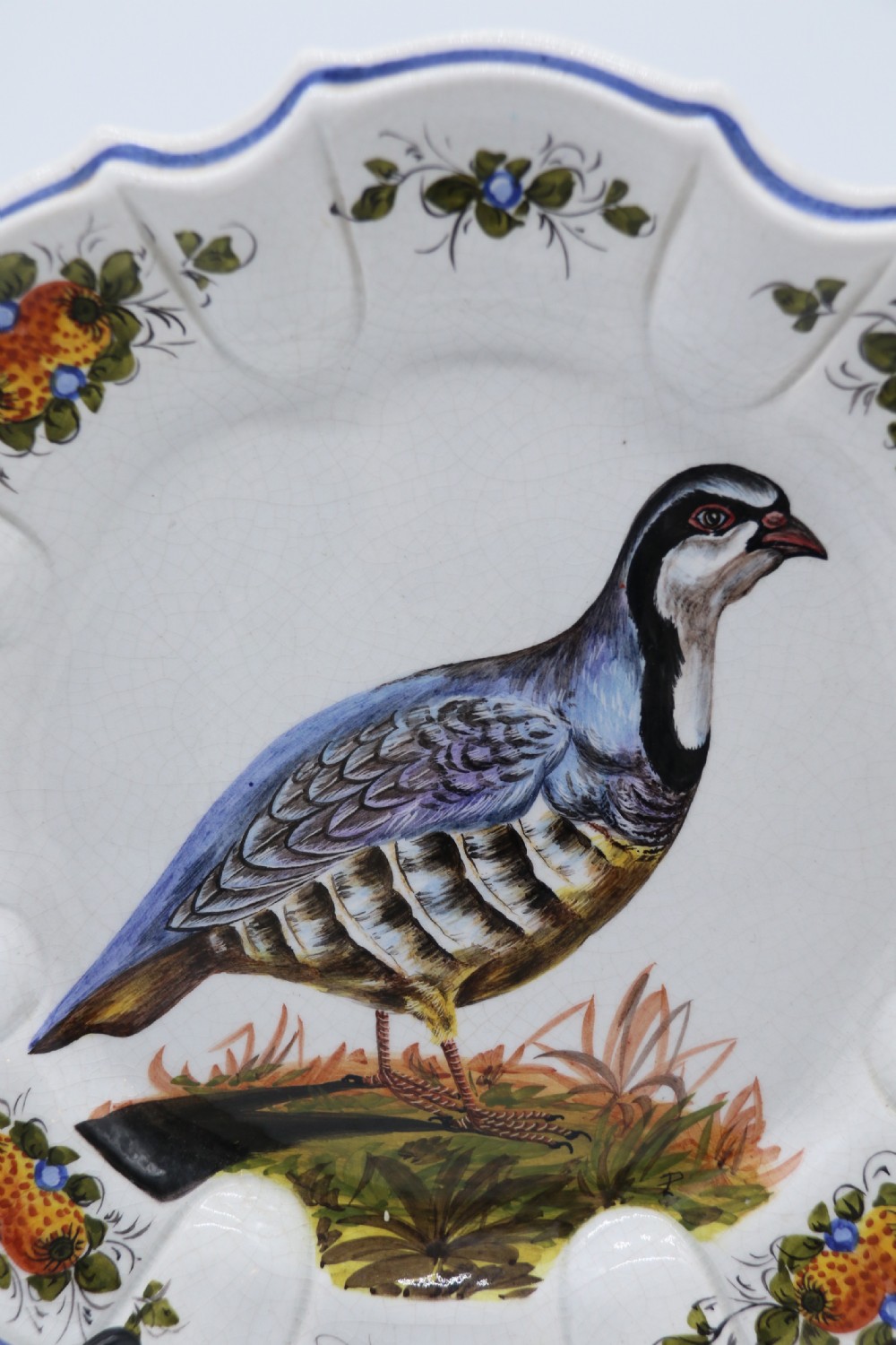 A circular tin-glazed earthenware wall charger featuring a hand-painted game bird in the centre surrounded by a scalloped, floral-decorated rim with blue edging. View VIII