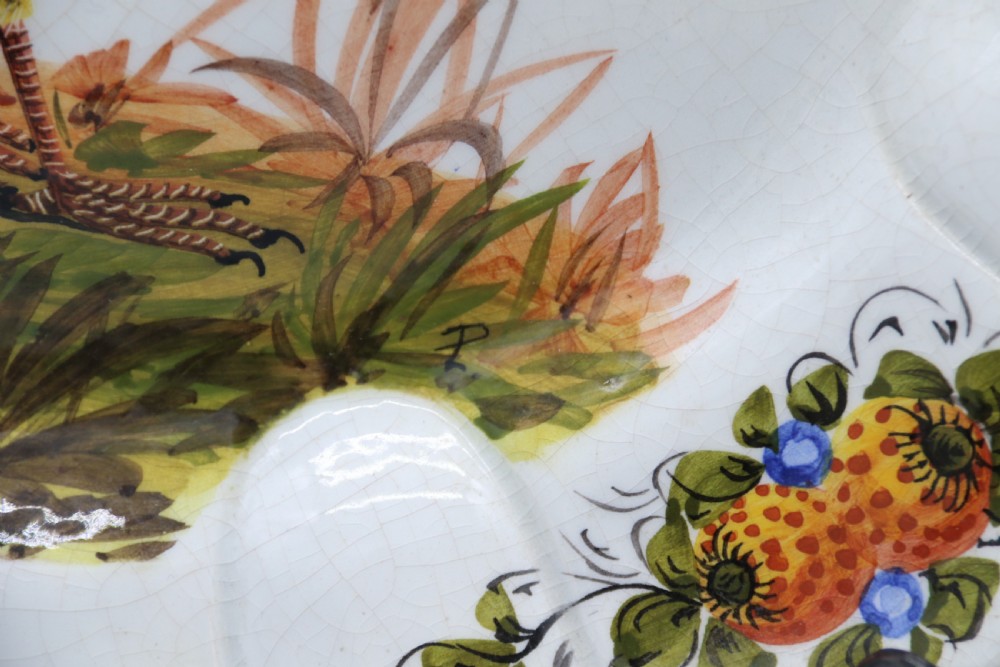 A circular tin-glazed earthenware wall charger featuring a hand-painted game bird in the centre surrounded by a scalloped, floral-decorated rim with blue edging. View IX