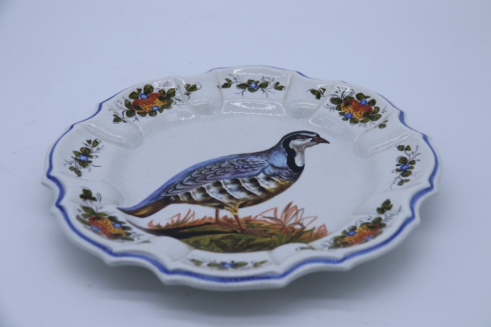 A circular tin-glazed earthenware wall charger featuring a hand-painted game bird in the centre surrounded by a scalloped, floral-decorated rim with blue edging. View XIII