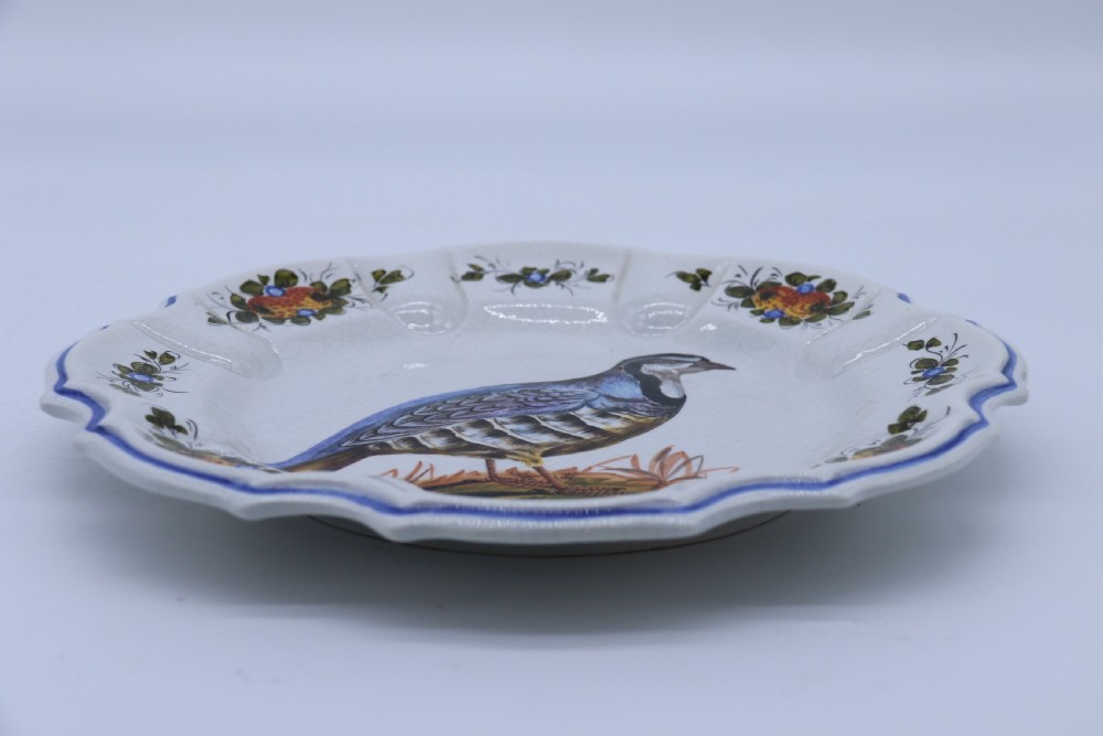 A circular tin-glazed earthenware wall charger featuring a hand-painted game bird in the centre surrounded by a scalloped, floral-decorated rim with blue edging. View XIV